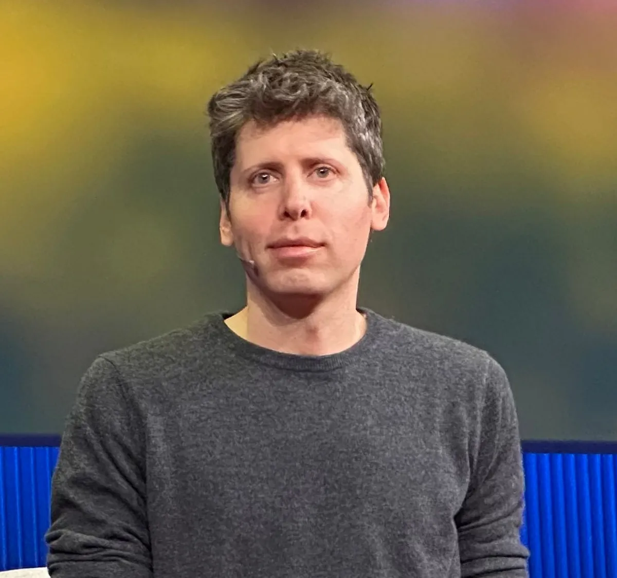 Sam Altman speaking on stage at TED in a grey sweater