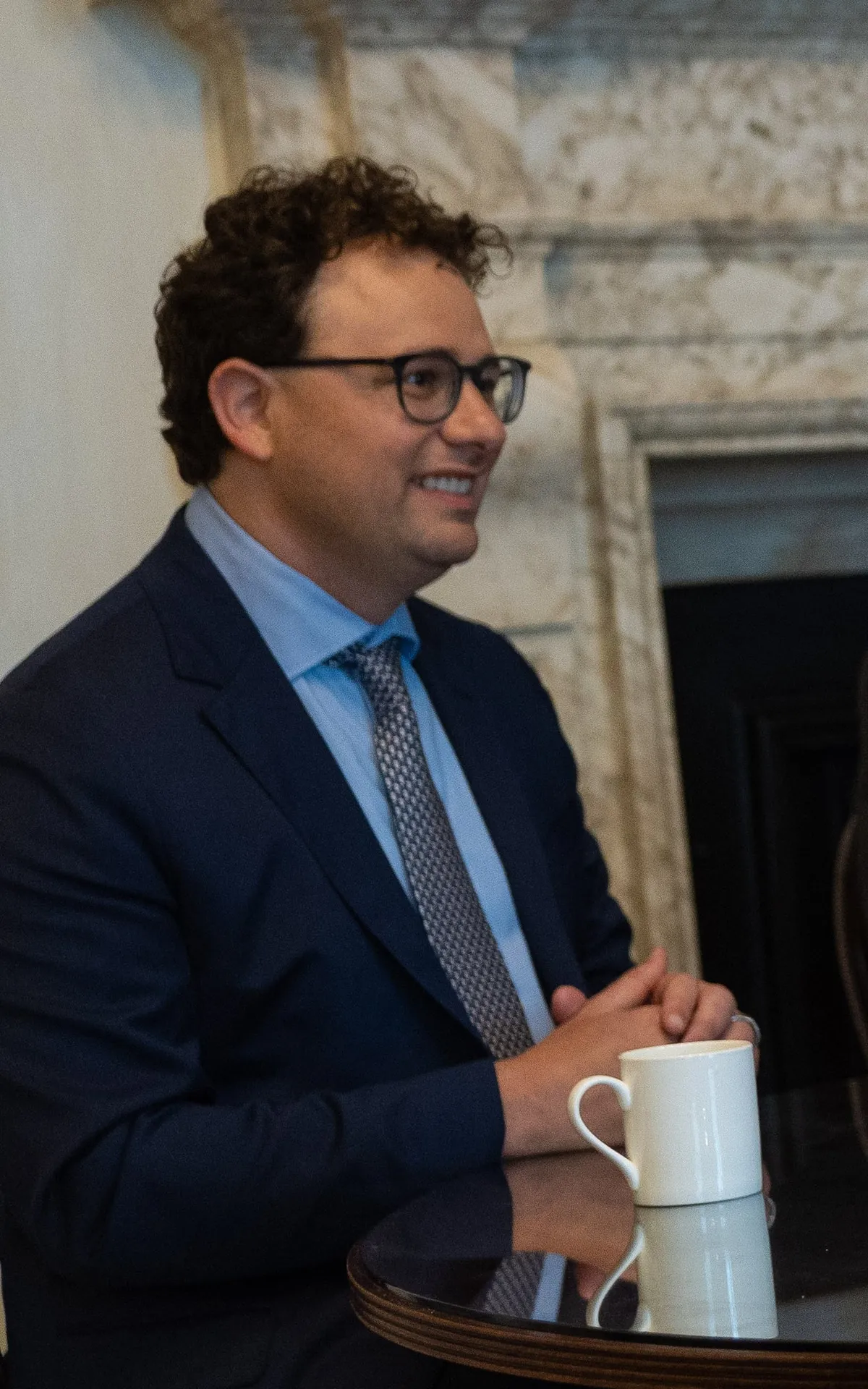 Dario Amodei in a suit, holding a cup, in a meeting room